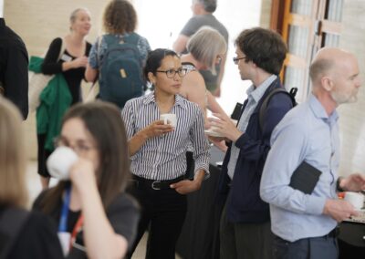 A man and a woman having a serious discussion, each holding a cup of coffee. They are surrounded by other people in business casual chatting and drinking.