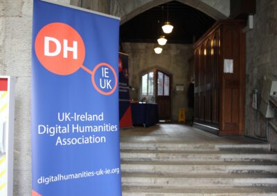 A blue and orange pop up banner for the UK-Ireland DH Association in front of a gray stone hallway.