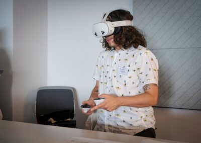 A delegate from the annual event in 2025 is seen in a white shit and with long hair. They are wearing a VR headset from one of the demonstrations exhibiting at the event.